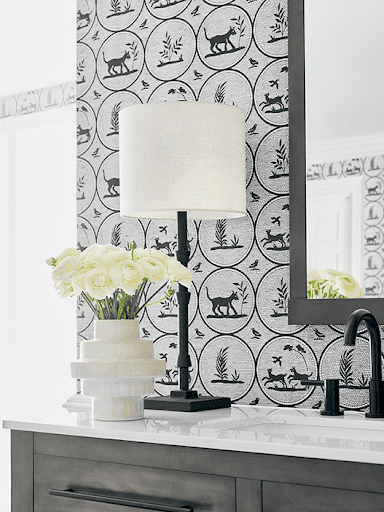 Grey wallpaper with patterns of dogs, birds, and plants line the walls of the a white and grey bathroom counter.